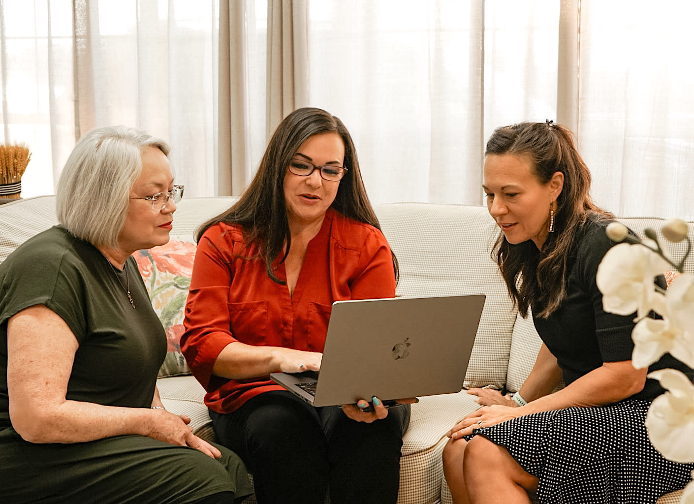 Cheyanne Marston in a red shirt, smiling with two clients as they view information on a laptop computer