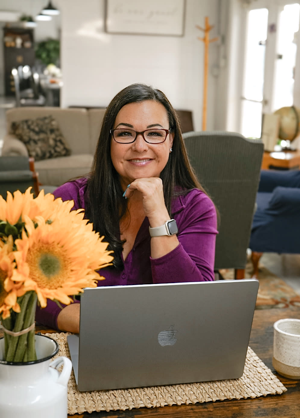 Cheyanne Marston, smiling and sitting at a laptop on a desk with yellow flowers